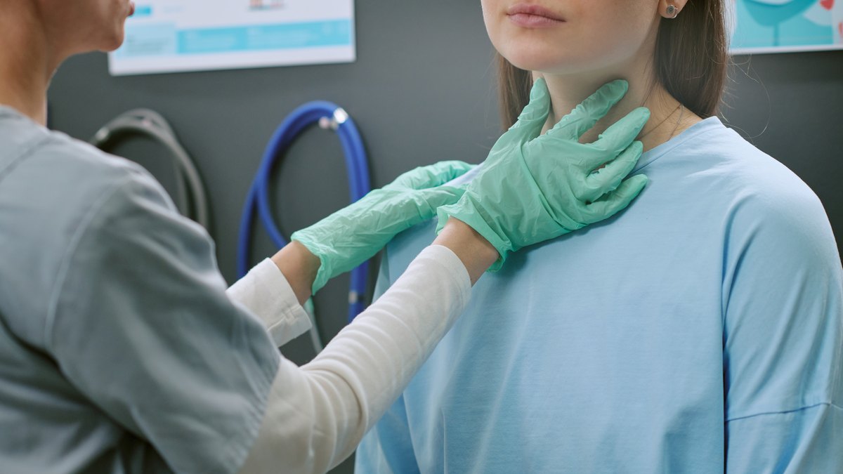 Medic examinând tiroida unei paciente, prin palpare