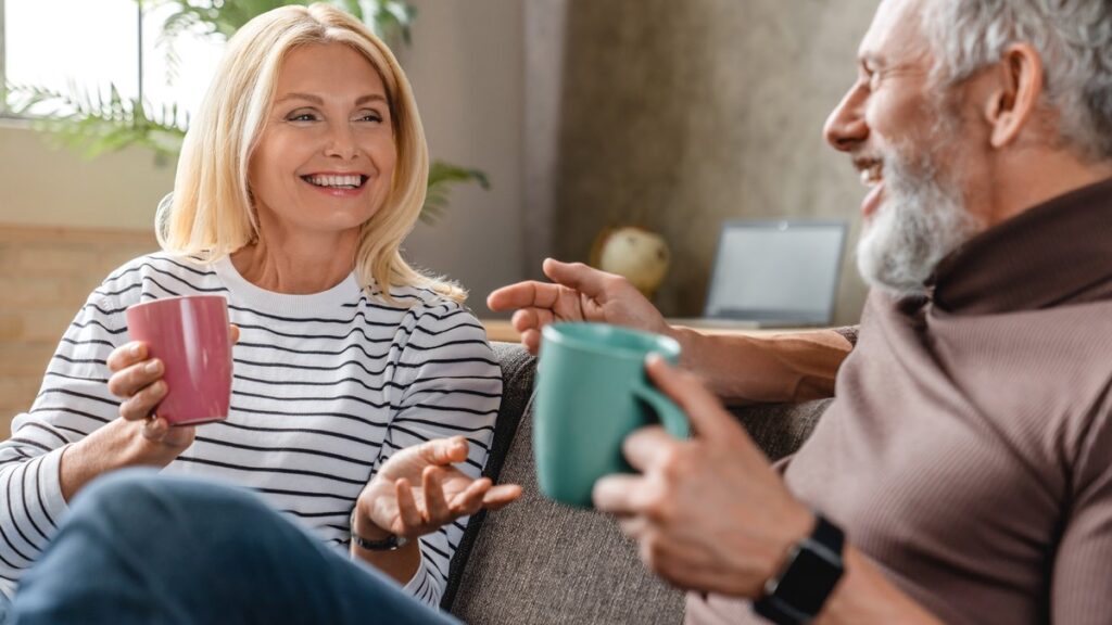 Cuplu matur discutând relaxat cu cănile de cafea în mână